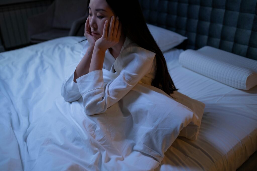 An Asian woman in bed at night, experiencing insomnia and loneliness, deep in thought.